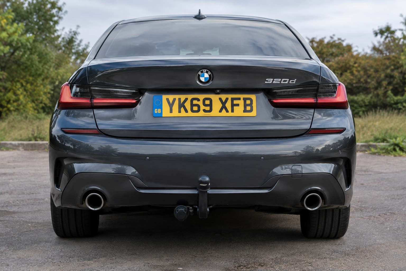Rear view of a dark grey BMW 320d with a towbar installed, parked outdoors.